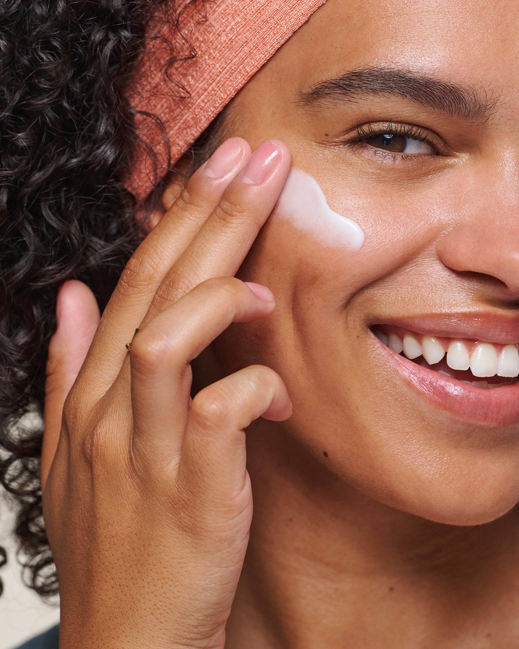 Close-up of smiling model applying Face Cream to cheek
