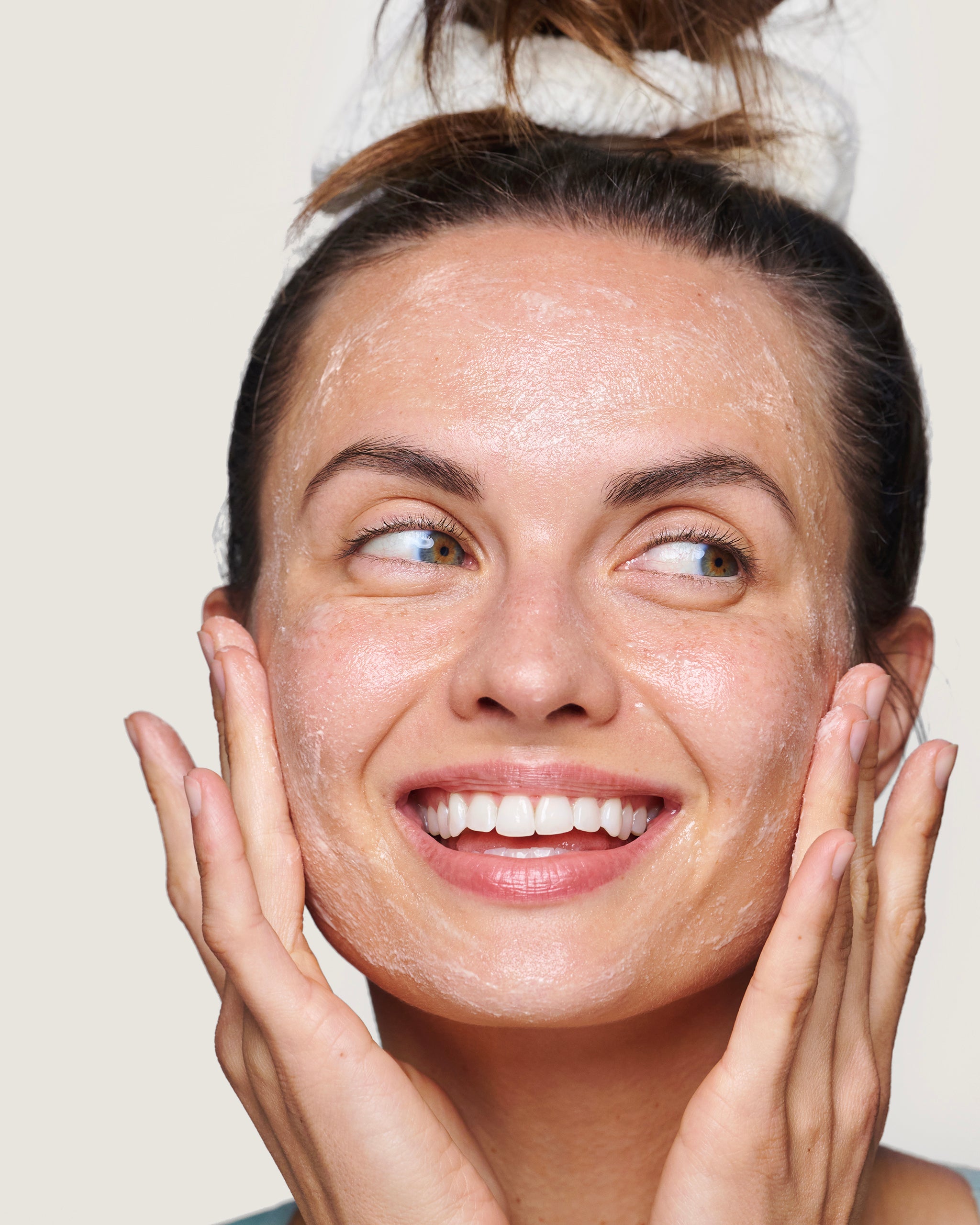 Image of smiling model massaging Microdermabrasion Facial into cheeks, with gray background