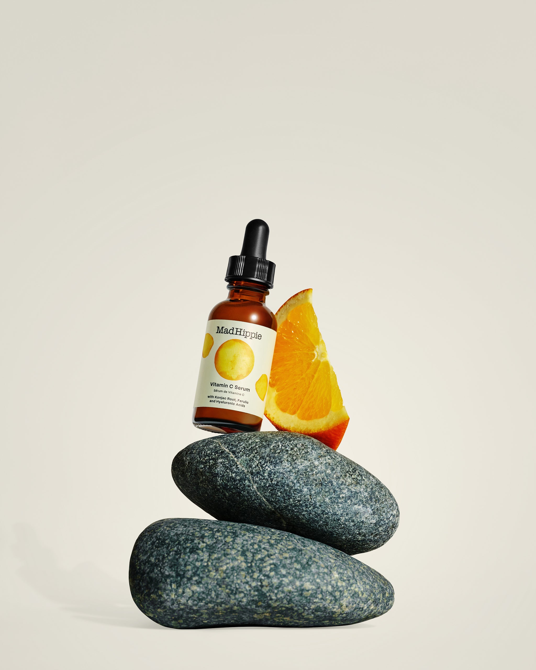 Vitamin C Serum bottle + orange wedge sitting on two granite rocks, with gray background