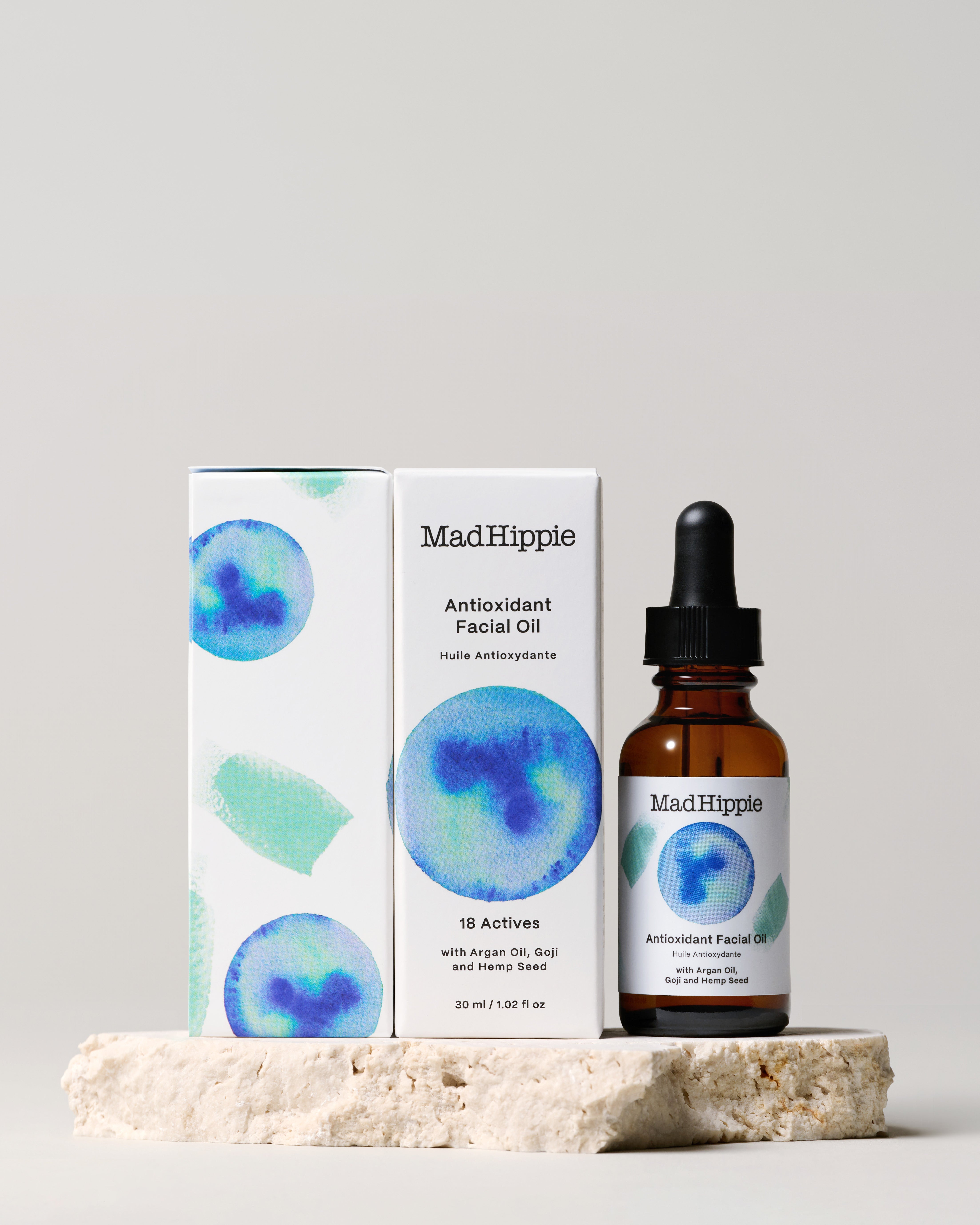 Antioxidant Facial Oil bottle + two boxes on stone slab, with gray background