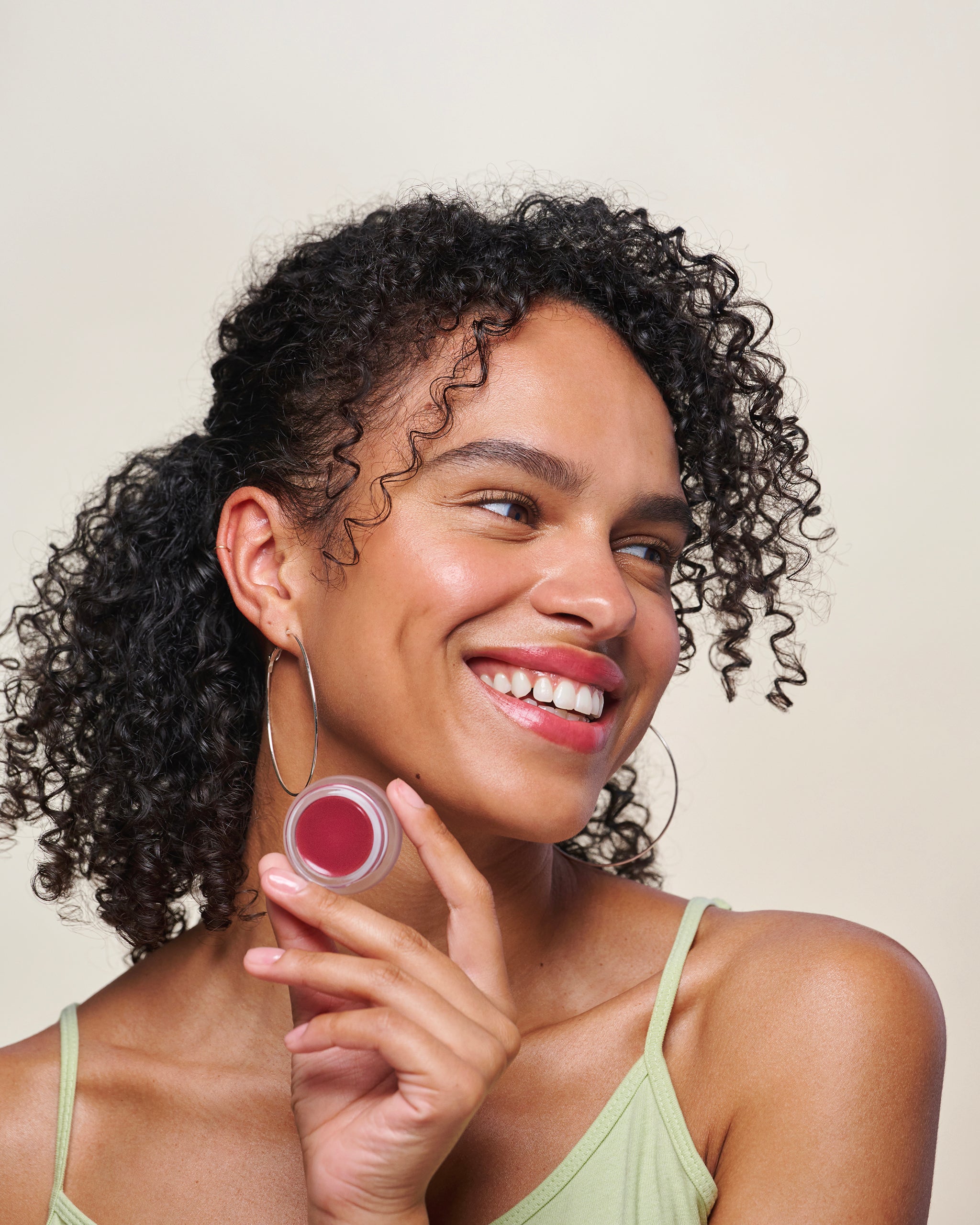Model smiling and holding Cheek & Lip Tint, with gray background