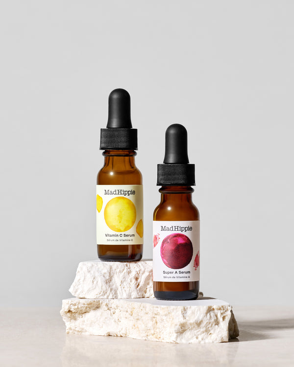 Bottles of Vitamin C Serum + Super A Serum on stone slabs, with grey background