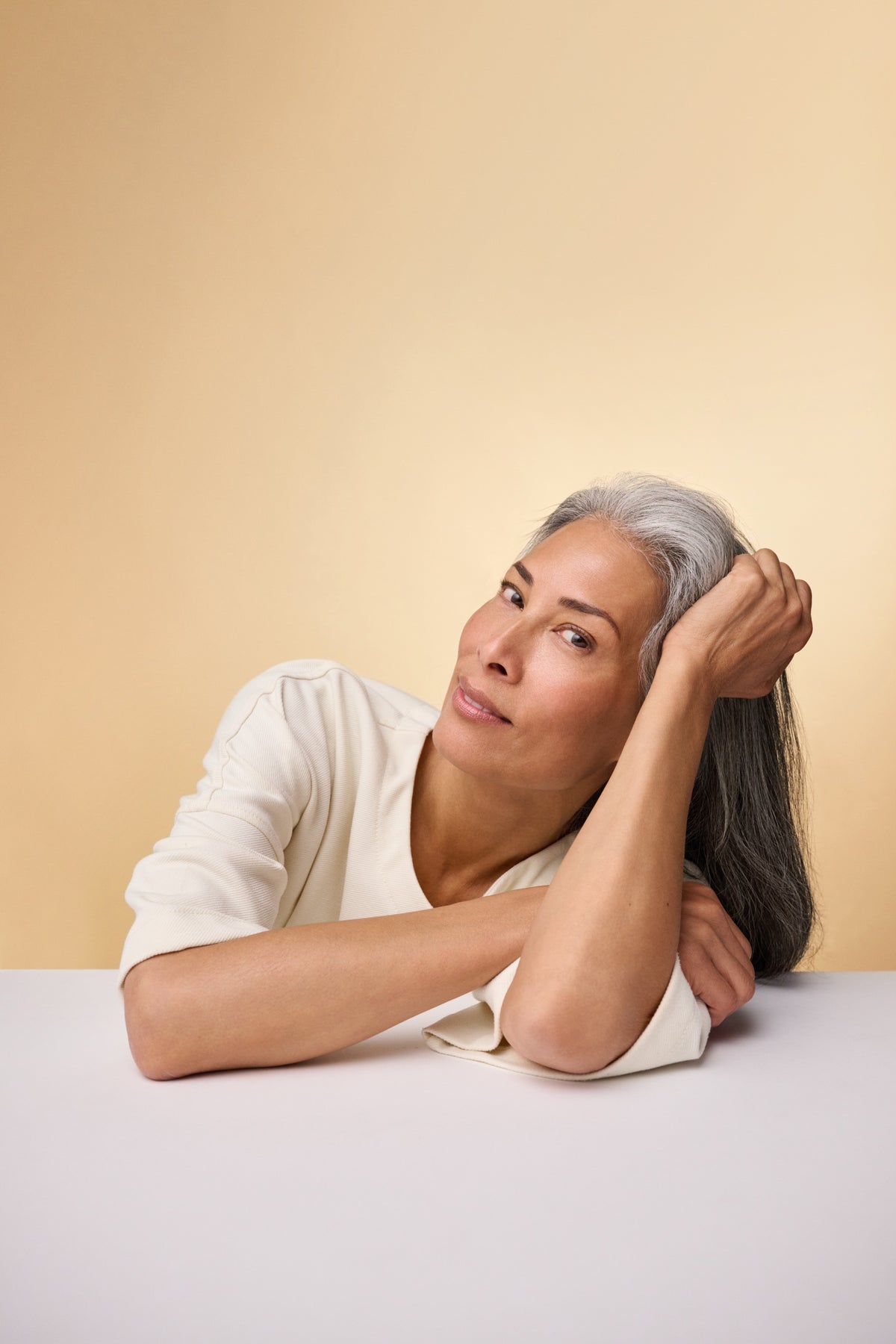 Silver-haired woman leaning on a table, smiling at the camera